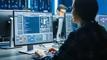 Person working on multiple computer screens in a dark office.