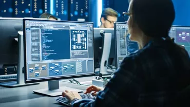 Person working on multiple computer screens in a dark office.