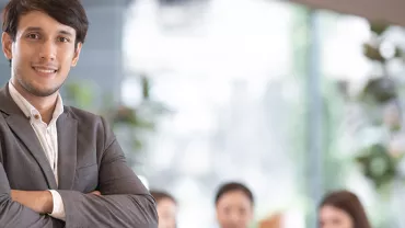 Confident businessman with arms crossed, standing in a bright office.