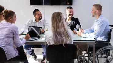 A diverse group of colleagues smiling in a meeting around a glass table.