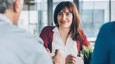Woman smiling in a meeting with two people in an office setting.