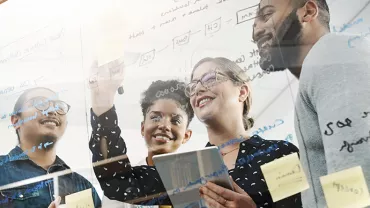 Group of people brainstorming with notes on glass board.