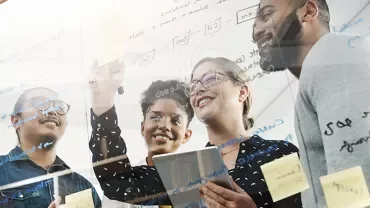 Group of people brainstorming with notes on glass board.