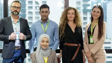 A diverse group of five people smiling in a modern office setting.