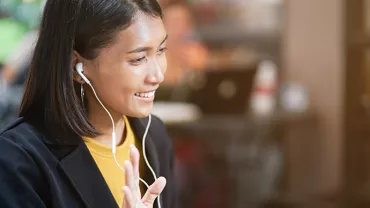 Woman wearing earbuds, smiling in a cafe during a video call.