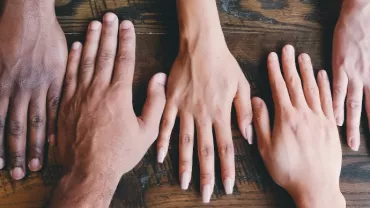 Five diverse hands placed on a wooden table.