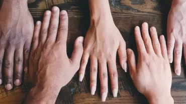Five diverse hands placed on a wooden table.