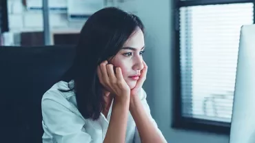 Woman sitting at a desk, looking at a computer screen with focus.