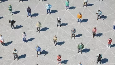 Aerial view of people standing on a geometric pattern on concrete, each casting a shadow.