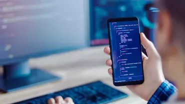 Person holding a smartphone with code visible on the screen.
