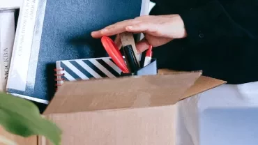 Person packing office supplies in a cardboard box.