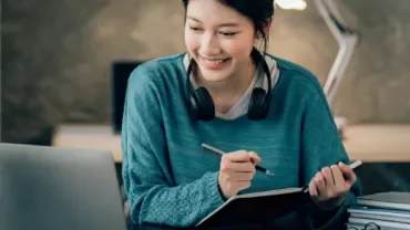 Woman smiling while writing in a notebook at her desk