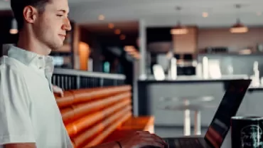 Man working on a laptop in a modern cafe setting.