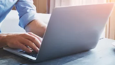 Person typing on a laptop at a wooden table with a cup of coffee.