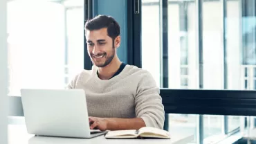 Man smiling while working on a laptop at a desk.