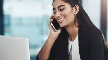 Woman in an office talking on the phone while using a laptop.