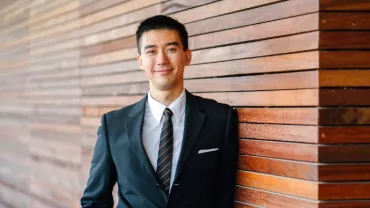 Asian man in a business suit standing against a wall