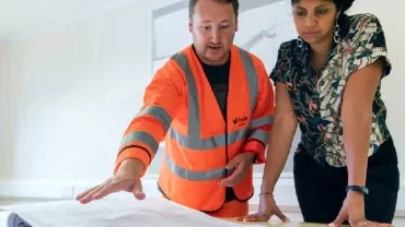 Two people reviewing a large blueprint on a table.