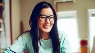Smiling person with glasses using a laptop at home.