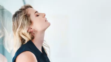 Side profile of a woman leaning against glass, eyes closed, appearing relaxed.