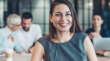 Smiling woman in a business meeting with colleagues in the background.