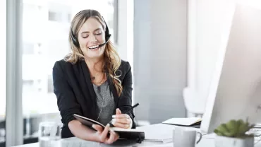 2. A woman wearing a headset holds a notepad, engaged in a discussion or taking notes.
