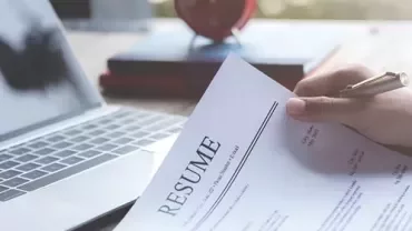 A person holding a resume in front of a work device