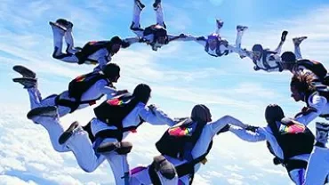 Group of skydivers forming a circle in the sky against a backdrop of clouds on a sunny day.