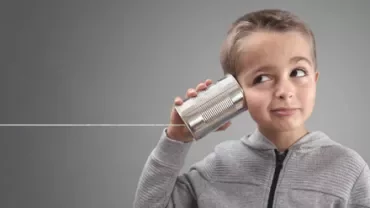 Child listens with a tin can telephone, string pulled taut.