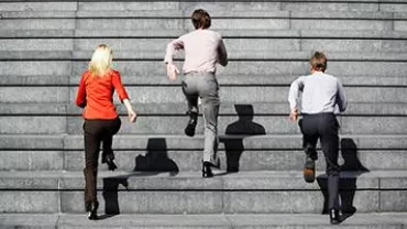 Three people in business attire running up a large set of stairs.