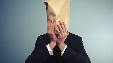 Person in a suit with a paper bag over their head, against a plain background.