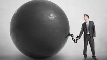 Man in business suit chained to a large black ball.