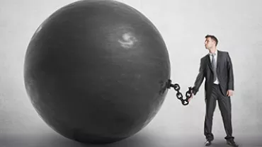 Man in business suit chained to a large black ball.