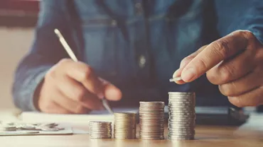 Person stacking coins in ascending order on a desk, emphasizing savings and financial planning.