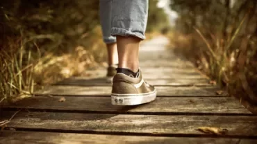 Person walking on a wooden path in nature, wearing casual sneakers and jeans.
