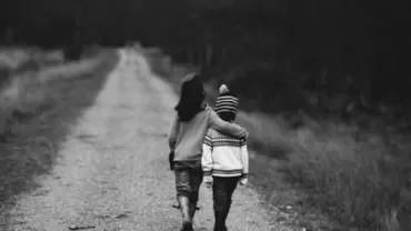 Two children walking on a rural path, one with an arm around the other, in black and white.