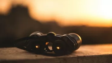 Binoculars on a ledge at sunset with a blurred background.