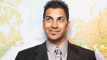 Smiling man in a suit stands in front of a world map.