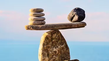 Stones balanced on a rock, with a clear blue sky and sea in the background.