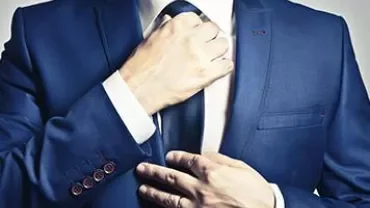 Person in a blue suit adjusting a tie.
