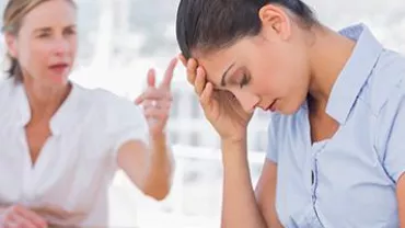 A woman sits with her head in her hand while another woman speaks to her in the background.