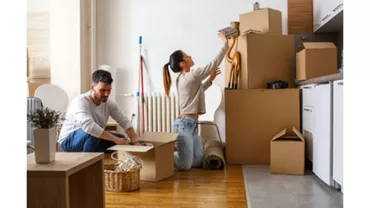 A couple unpacking boxes in a room with wooden floors.