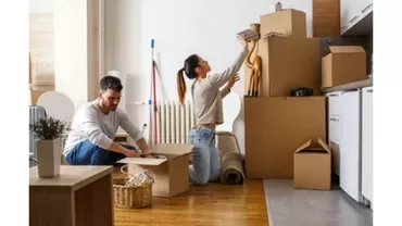 A couple unpacking boxes in a room with wooden floors.