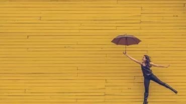 Person holding an umbrella and jumping against a yellow wooden wall.