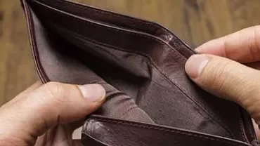An open, empty brown wallet held in hands over a wooden surface.