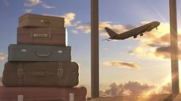 Stack of suitcases by an airport window with a plane taking off at sunset.