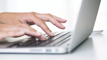 Person typing on a laptop keyboard with white background.