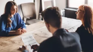 Woman in blue at a job interview with two interviewers at a wooden table.