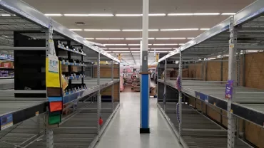 Empty store shelves with sparse items, wide aisle in a supermarket.