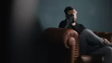 Man sitting on a leather couch with his hand on his face, looking tired.